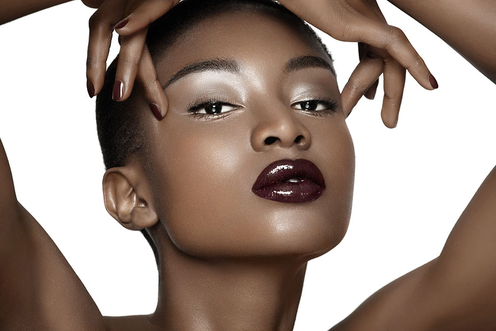 Beautiful African fashion model closeup. Plum lipstick and dark nail polish. Posing over white background.